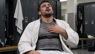 Sweaty grappler in a locker room after training, hand on his chest over a heart rate strap
