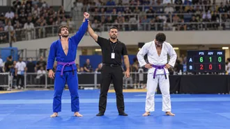 Referee raising the arm of a purple belt in a blue gi after a BJJ match, with the scoreboard showing points, advantages and penalties