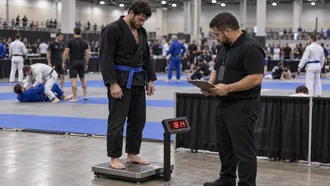 BJJ competitor in a black gi standing on a digital scale at a tournament weigh-in while an official checks the reading