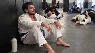 Sweaty blue belt smiling against the academy wall between rounds at open mat
